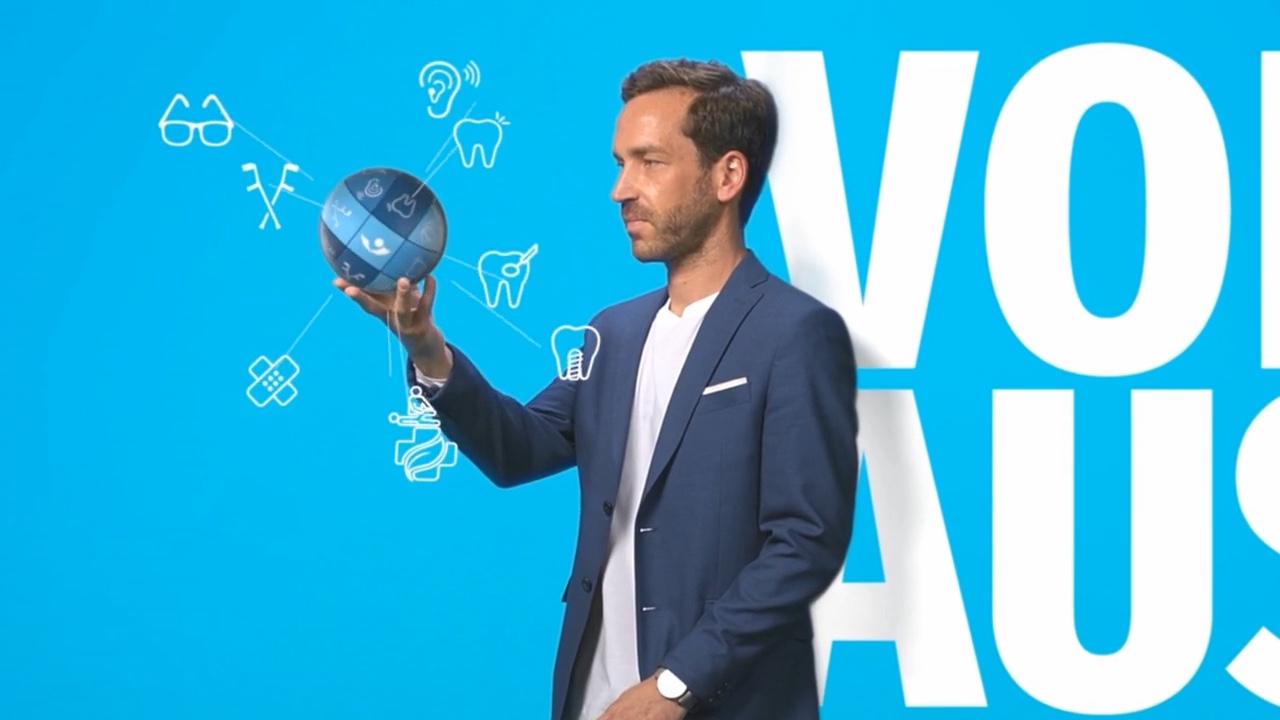 Man in front of a blue background holding a glowing sphere with icons, next to the word “Voraus”